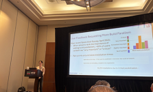 Kathleen presenting at a podium in front of a big screen, which shows a slide titled “User Feedback Requesting More Build Parallelism”